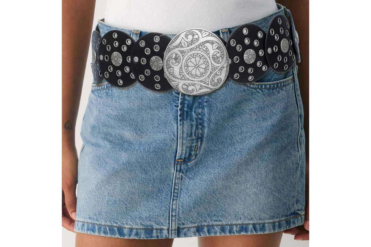 Model wearing a black concho belt with an oversized silver-tone buckle over a denim skirt