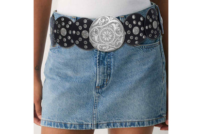 Model wearing a black concho belt with an oversized silver-tone buckle over a denim skirt