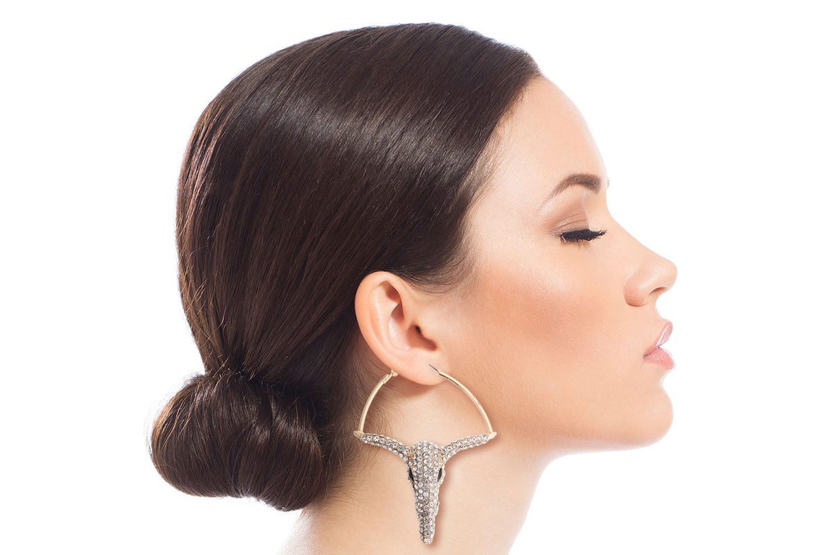 Model in profile wearing gold-tone hoop earrings with a rhinestone longhorn