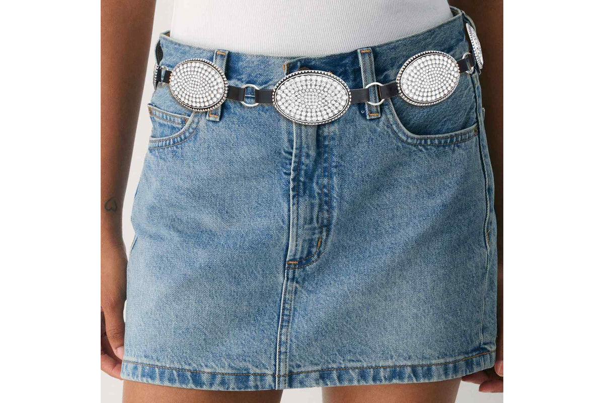 Model wearing a rhinestone oval concho chain belt over a denim skirt