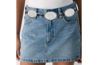 Model wearing a rhinestone oval concho chain belt over a denim skirt